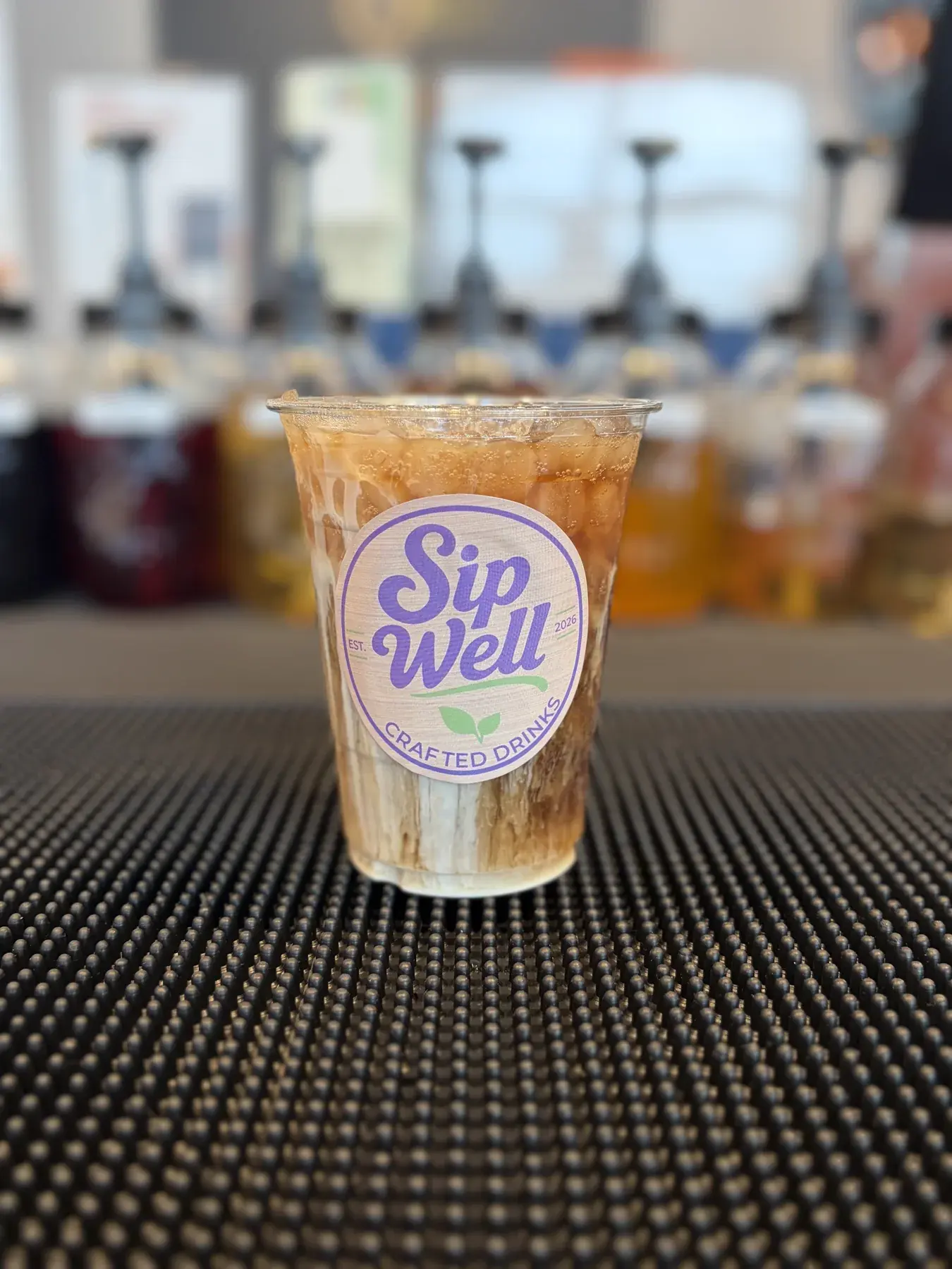 A Sip Well drink in a clear cup with the Sip Well sticker, showing the layer line where cream meets soda over ice
