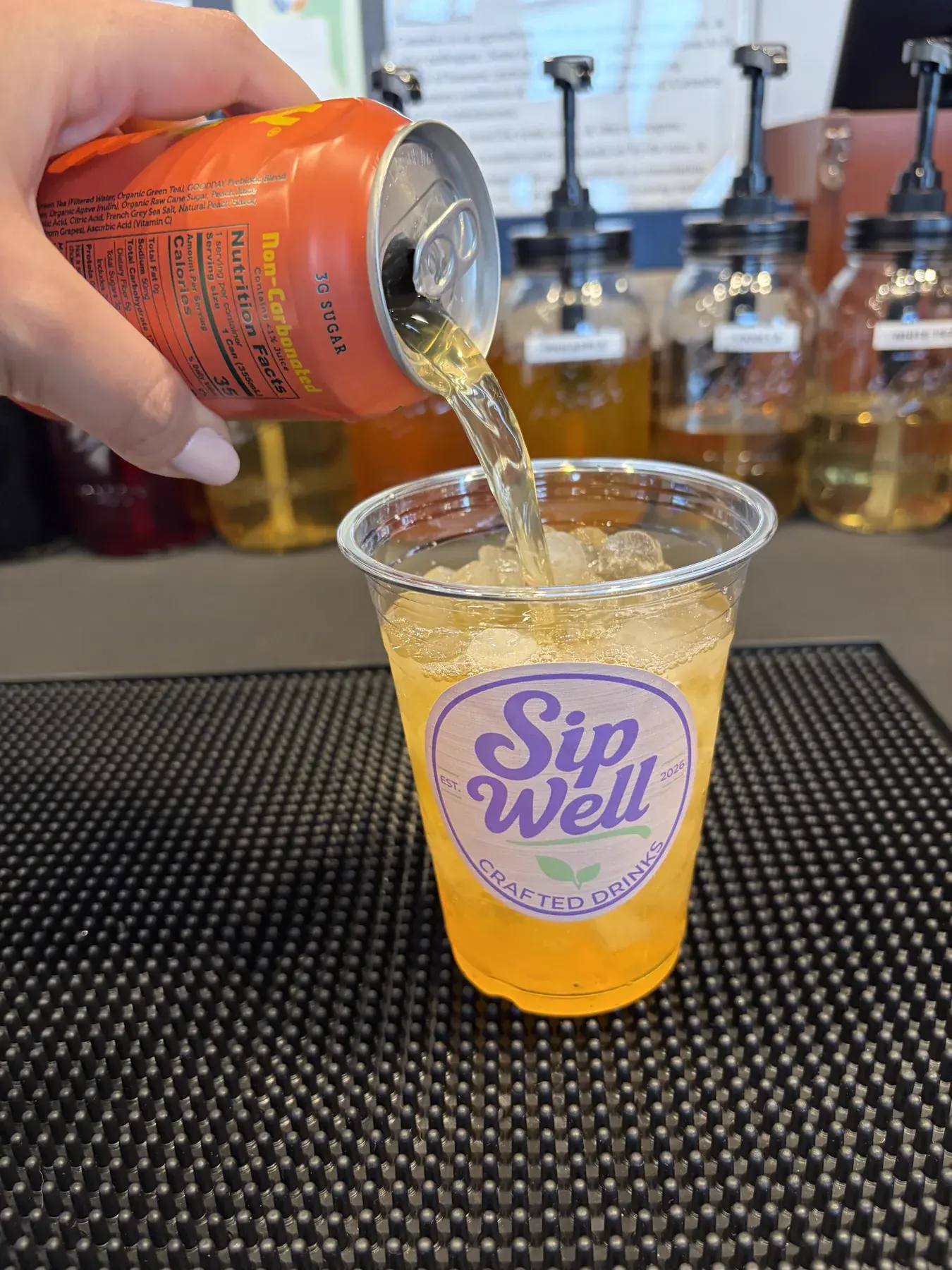 A can of Halfday peach iced tea being poured over ice into a Sip Well cup